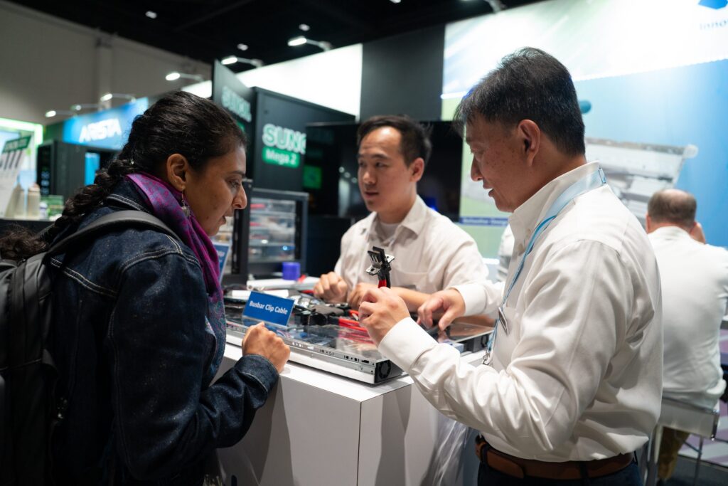 Exhibitors demonstrating hardware to a visitor on the expo floor at the 2025 OCP Global Summit