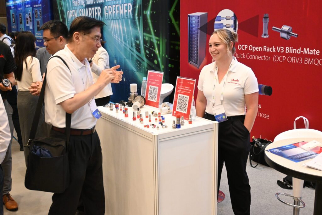 An exhibitor talking with a visitor at a booth at the 2025 OCP APAC Summit in Taipei